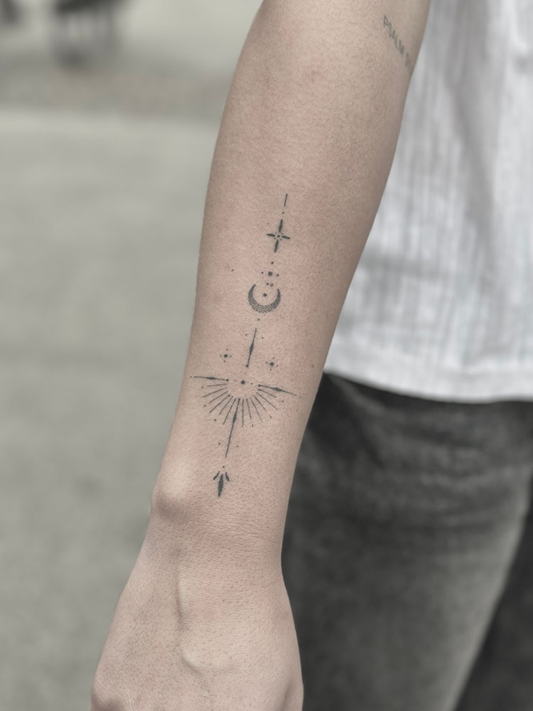 Fineline tattoo with a star, a moon and an arrow running the length of the forearm