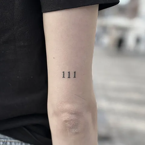 Lille fineline tatovering med tallet 111 på overarm