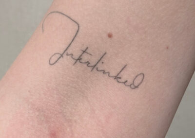 Helet fineline tatovering med håndskrevet ord på overarm