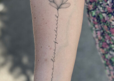 Fineline tattoo of a lotus flower with handwritten text down the forearm