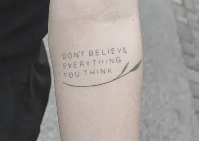 Fineline tekst-tatovering med et engelsk citat i versaler på overarm