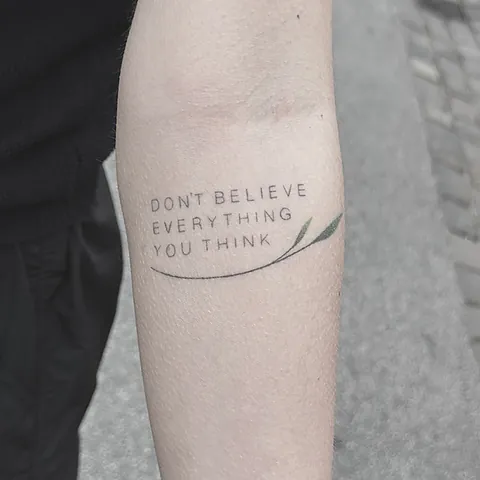Fineline tekst-tatovering med et engelsk citat i versaler på overarm