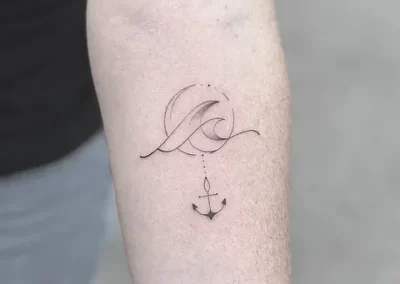 Fineline tatovering af bølge over et lille anker på underarm