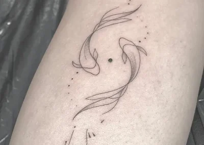 Fineline tatovering af to koifisk der svømmer om hinanden på overarm
