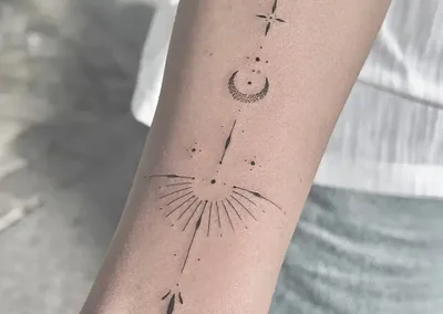 Fineline ornament med solstråler og pil på underarm, set tæt på