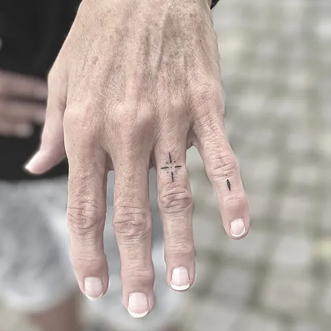 Fineline tattoos with small crosses and a star across the fingers