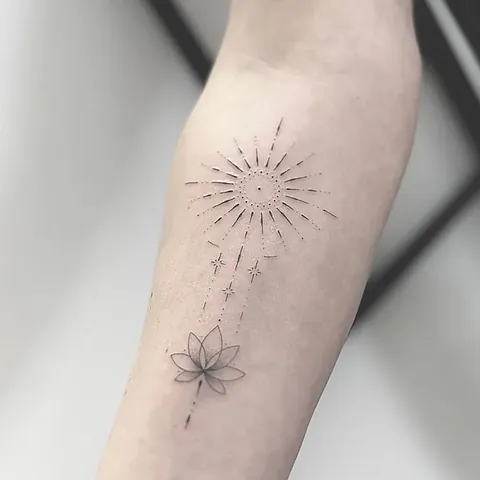 Fineline tattoo of a sun with rays above a lotus flower on the forearm