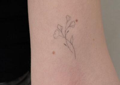 Helet fineline tatovering af blomstergren på overarm