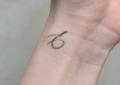 Helet fineline tatovering med håndskrevet initial på håndled