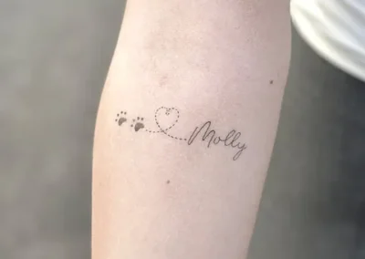 Fineline tatovering af hundepoter, hjerte og navnet Molly på underarm