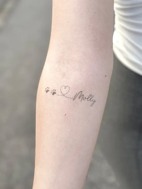 Fineline tatovering af hundepoter, hjerte og navnet Molly på underarm