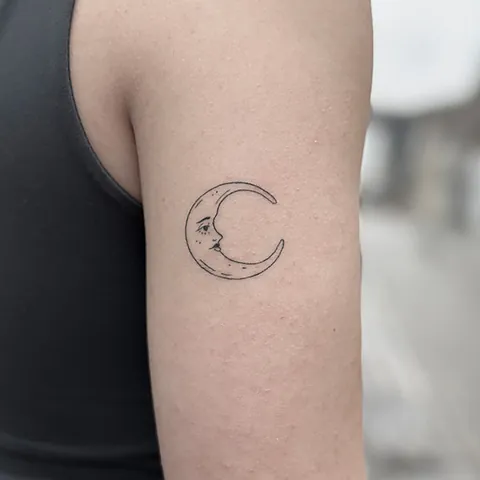 Fineline tatovering af halvmåne med ansigt på overarm