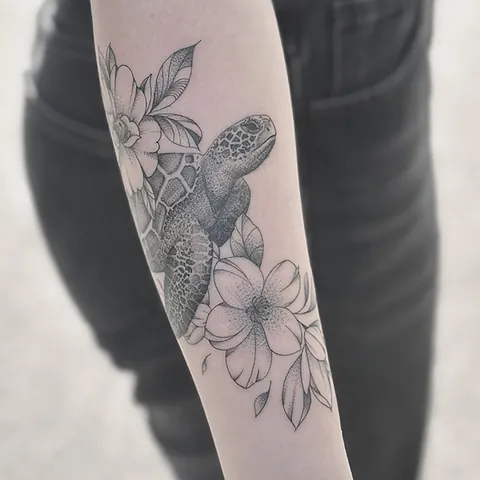 Skyggelagt tatovering af skildpadde omgivet af blomster på underarm