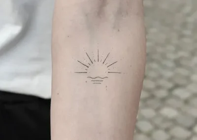 Fineline tatovering af solopgang med stråler på underarm
