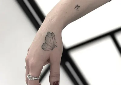 Fineline tatovering af sommerfugl på hånd med lille symbol på håndleddet