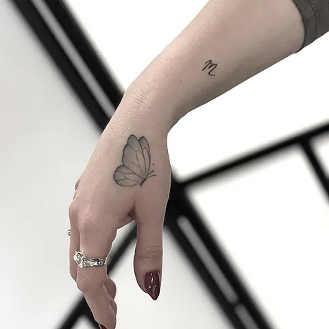 Fineline tattoo of a butterfly on the hand with a small symbol on the wrist