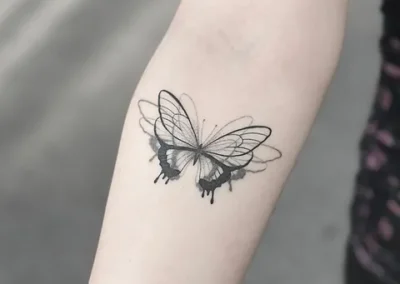 Skyggelagt tatovering af sommerfugl med mørke vinger på underarm