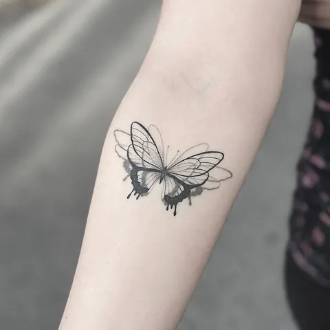 Skyggelagt tatovering af sommerfugl med mørke vinger på underarm