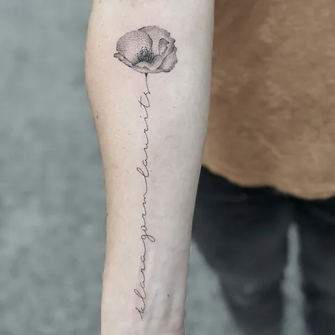 Fineline tatovering af valmue med håndskrevet tekst langs stilken på overarm
