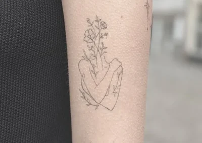 Fineline tatovering af en hånd der holder blomster på underarm