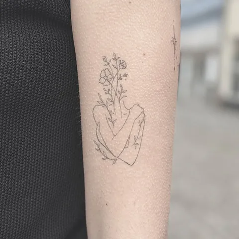 Fineline tatovering af en hånd der holder blomster på underarm