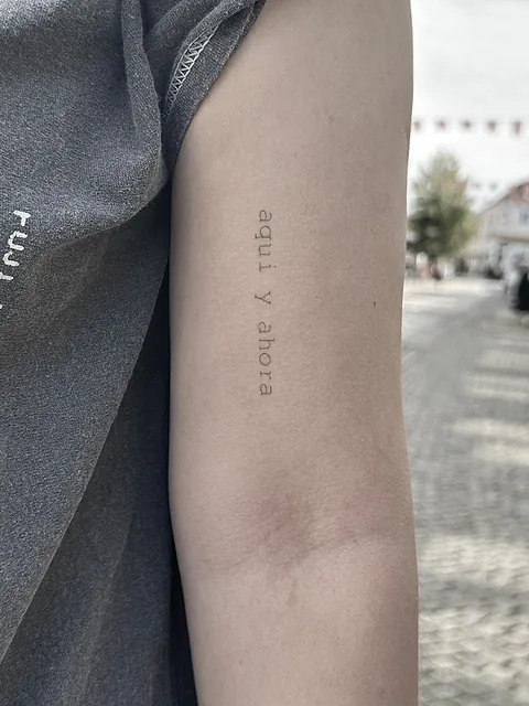 Fineline tekst-tatovering med spansk citat langs overarmen