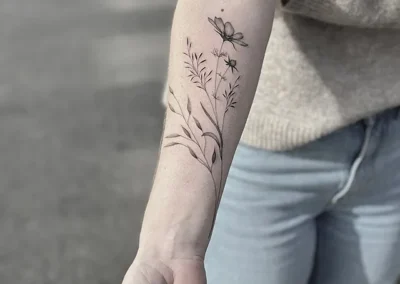 Fineline-tatovering med markblomster og strå op langs underarmen