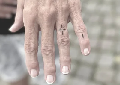 To små fineline-tatoveringer på fingrene, et kors og en lodret streg