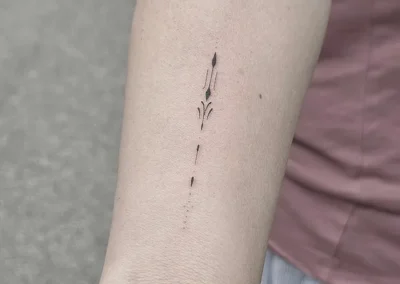 Fineline-tatovering med et smalt lodret ornament på underarmen