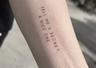 Fineline-tatovering med teksten Tell me a secret. A nice one. på underarmen