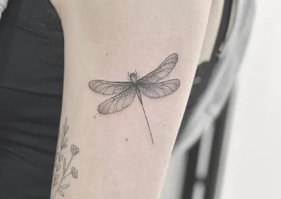 Fineline-tatovering af en guldsmed med små blomster på overarmen