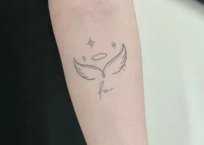 Helet fineline-tatovering med englevinger, glorie og ordet far på overarmen