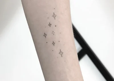 Helet fineline-tatovering med små spredte stjerner på underarmen