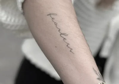 Helet fineline-tatovering med ordet fearless i håndskrift på underarmen