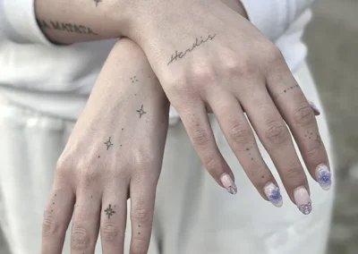 Helede fineline-tatoveringer med stjerner, prikker og skrift på hænder og fingre