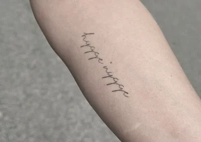 Helet fineline-tatovering med ordene hygge wygge i håndskrift på underarmen