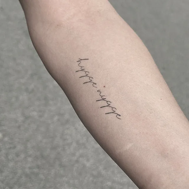 Healet – hygge wygge på underarm Helet fineline-tatovering med ordene hygge wygge i håndskrift på underarmen