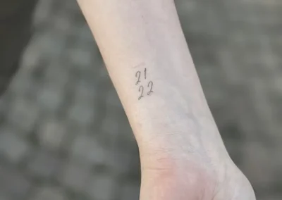 Helet fineline-tatovering med tallene 21 og 22 på håndleddet