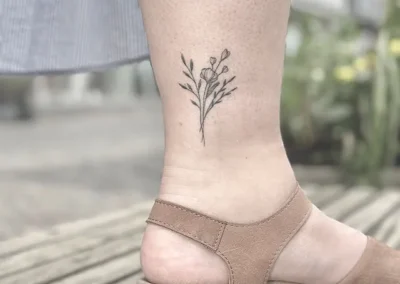 Helet fineline-tatovering af en blomstergren på anklen