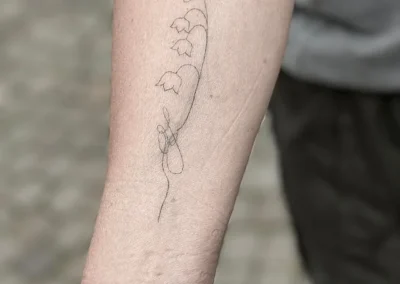 Helet fineline-tatovering af liljekonvaller på underarmen