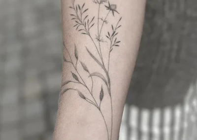 Helet fineline-tatovering med markblomster og strå på underarmen