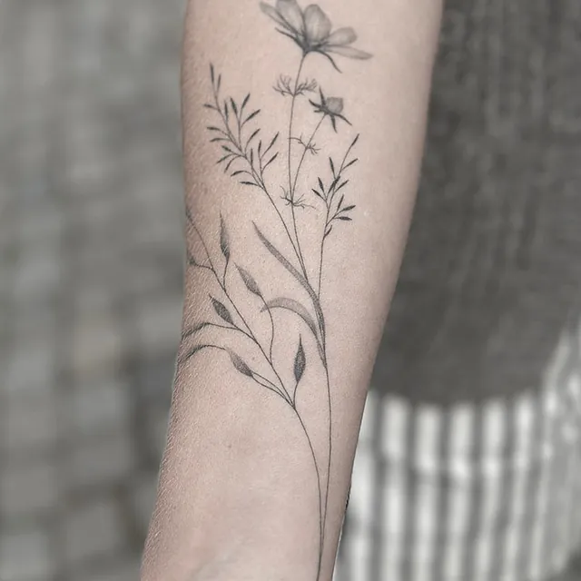 Healet – markblomster på underarm Helet fineline-tatovering med markblomster og strå på underarmen