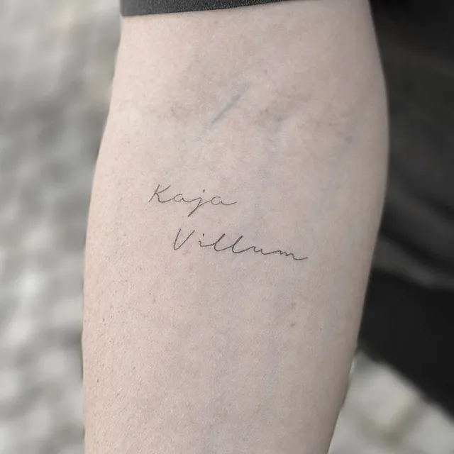 Healet – navnene Kaja og Villum Helet fineline-tatovering med navnene Kaja og Villum i håndskrift på overarmen
