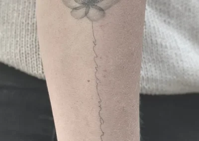 Helet fineline-tatovering af en blomst med håndskrevet tekst ned ad underarmen