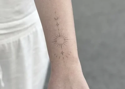 Helet fineline-tatovering med en sol med stråler og en måne på underarmen