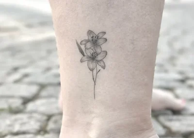 Helet fineline-tatovering af en lilje på anklen