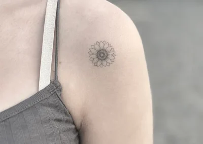 Helet fineline-tatovering af en solsikke på skulderen