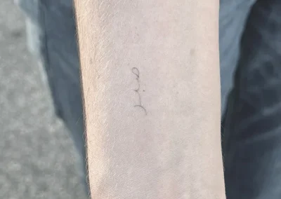 Helet fineline-tatovering med lille håndskrift på underarmen