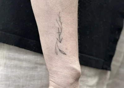 Helet fineline-tatovering af en gren med blade på underarmen