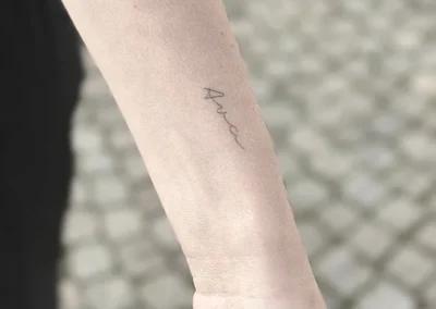 Helet fineline-tatovering med et håndskrevet ord på underarmen